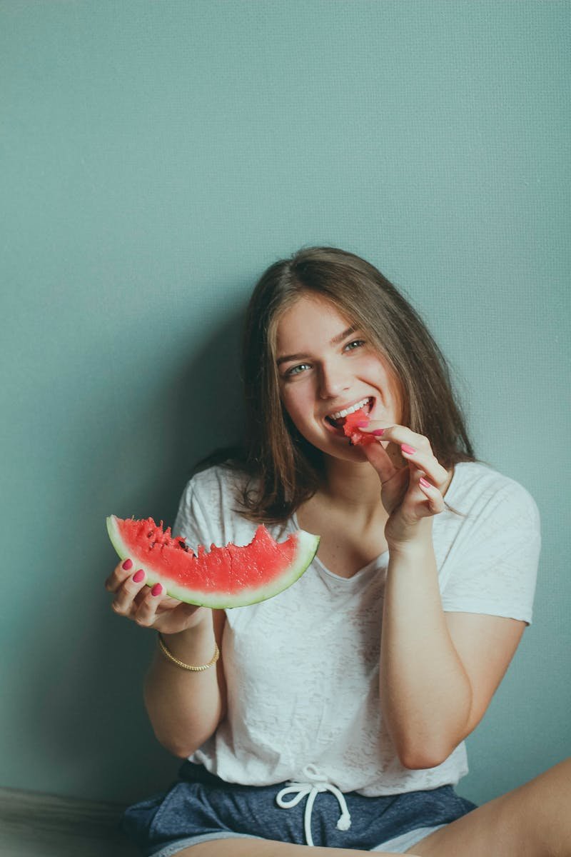 Smiling young woman sitting indoors enjoying a fresh slice of watermelon.