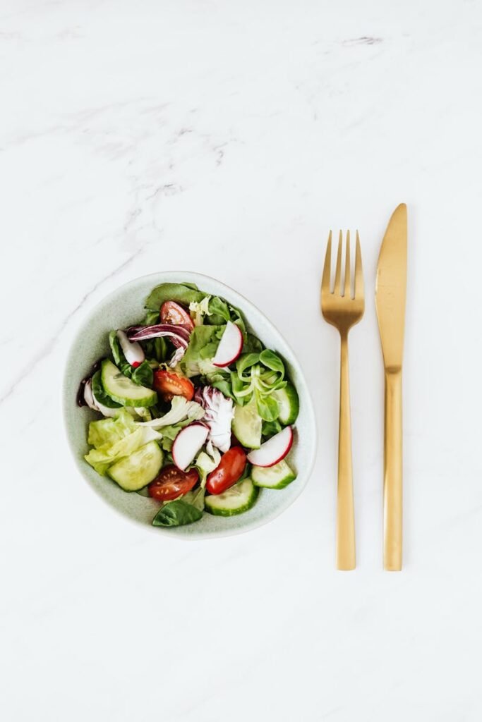 pexels-photo-4198023-4198023 Bowl of fresh vegetable salad with golden cutlery on a marble surface, healthy meal concept.
