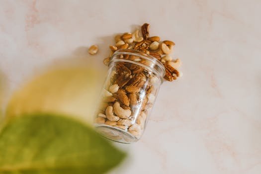 A glass jar spilling mixed nuts including cashews and almonds on a marble surface.